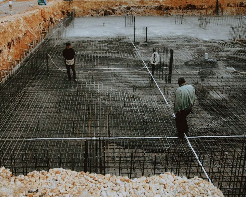 Ferralla de una losa de cimentación montada sobre el terreno, con dos operarios trabajando encima de la malla de acero