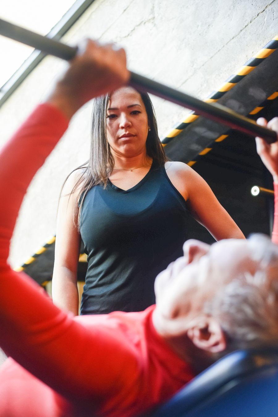 Una entrenadora asegura la barra mientras un socio mayor hace press de banca con la técnica correcta