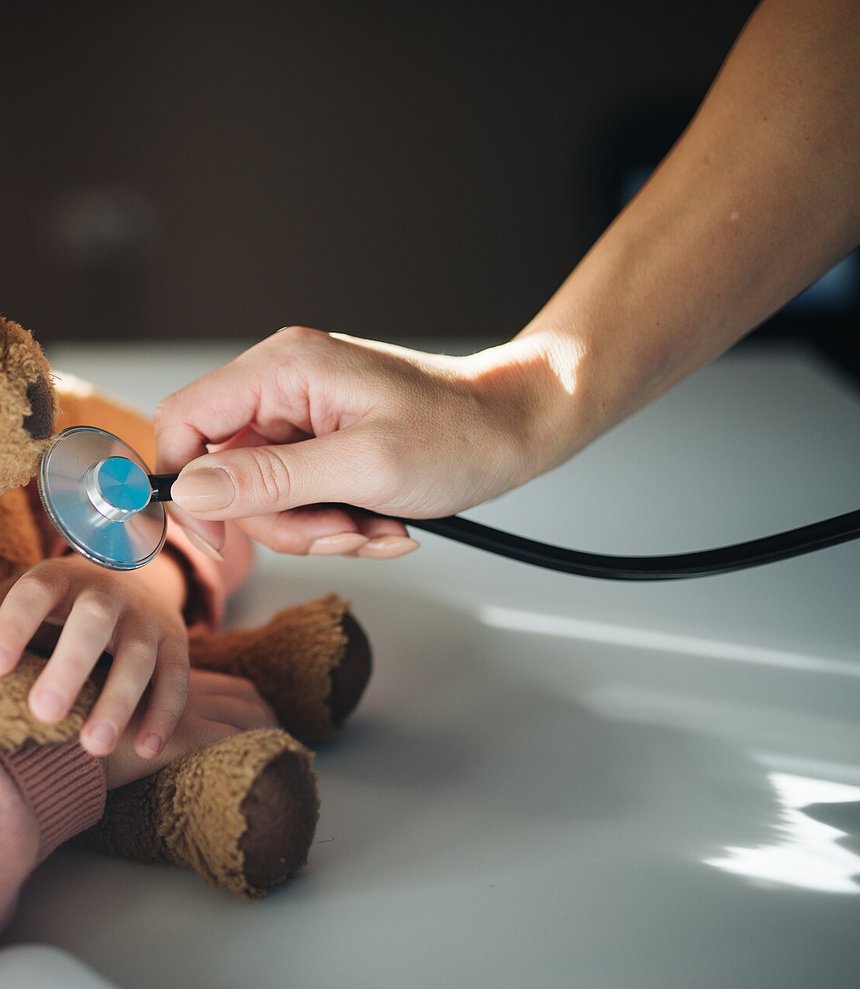 Manos de un pediatra auscultando un peluche con un fonendoscopio antes de la revisión